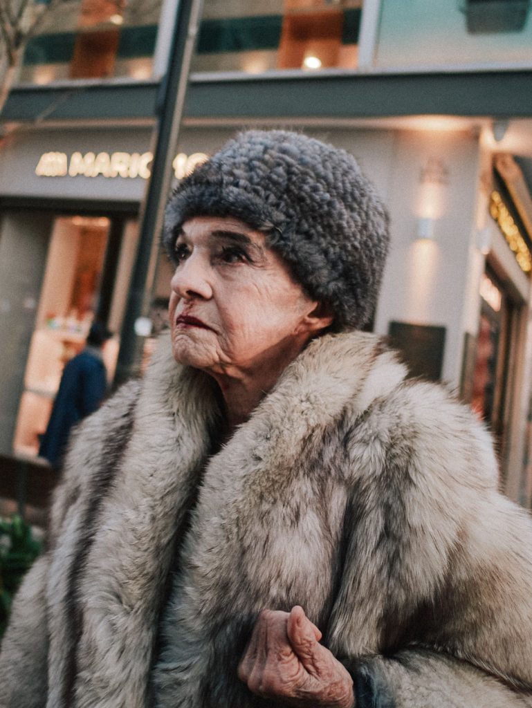 Close-up street documentary portrait of an elderly woman wearing a fur coat and grey wool hat